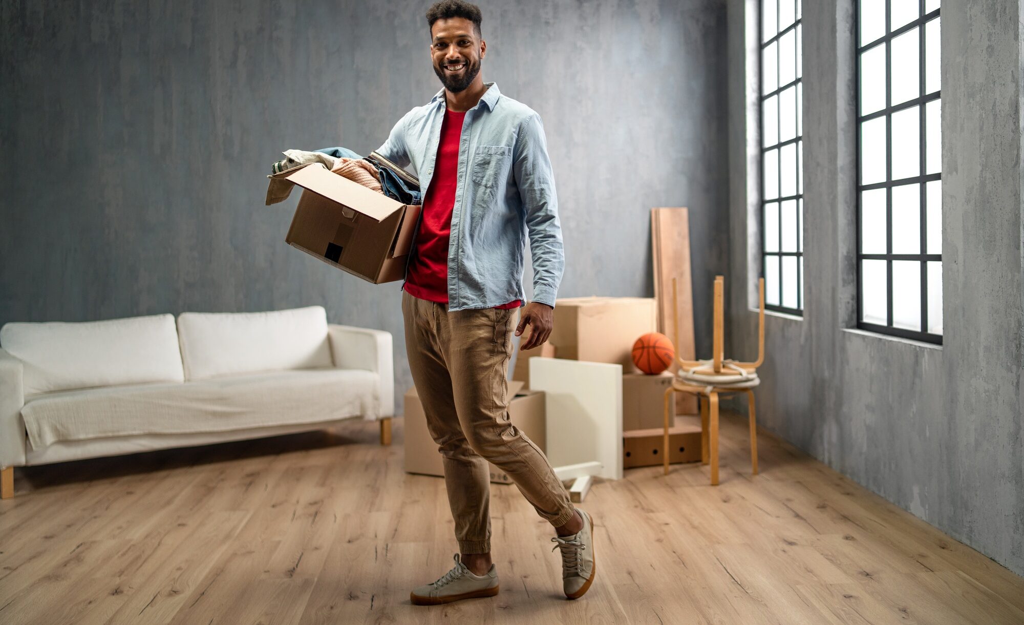 Happy young man holding packing boxes moving home, looking at camera, new living concept.